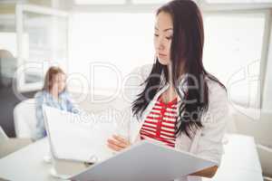 Businesswoman holding files with colleague in background at offi