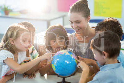 Teacher looking at schoolchildren touching globe