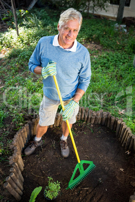 Portrait of happy gardener using rake at garden