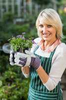 Happy mature female gardener holding potted flowers