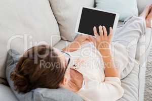 Woman using digital tablet while resting on sofa