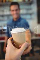 Close-up of customer taking coffee from barista at cafe