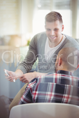 Businessman holding mobile phone while discussing with colleague