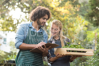 Man writing on clipboard while gardener holding plants