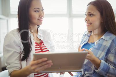 Close-up of colleagues discussing with digital tablet in office
