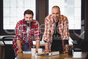 Confident creative coworkers leaning at desk in office