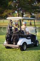 Rear view of male golfer friends sitting in golf buggy
