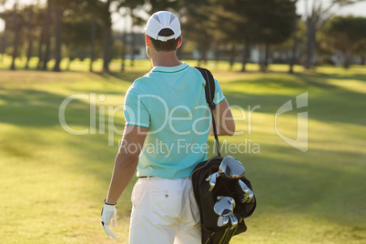 Rear view of golf player carrying bag