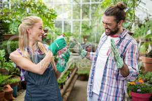 Cheerful gardener spraying water on colleague at greenhouse