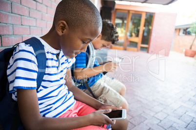 Schoolboys using mobile phones at corridor in school