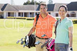 Portrait of couple carrying golf bags