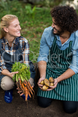 Coworkers holding harvested vegetables on field