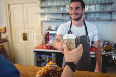 Happy barista offering coffee in disposable cup to customer at c