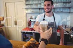 Happy barista offering coffee in disposable cup to customer at c