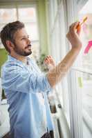 Businessman sticking adhesive notes on window at creative office