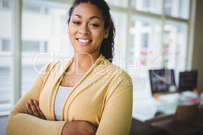Confident young businesswoman with arms crossed in creative offi