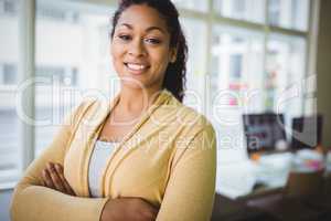 Confident young businesswoman with arms crossed in creative offi