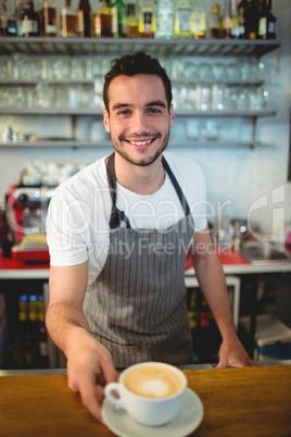 Portrait of happy barista offering coffee at cafeteria
