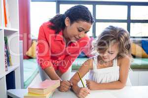 Teacher assisting girl writing on notebook in library
