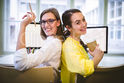 Portrait of happy colleagues sitting back to back at office
