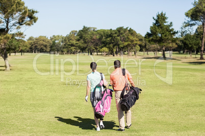 Rear view of couple carrying golf bags