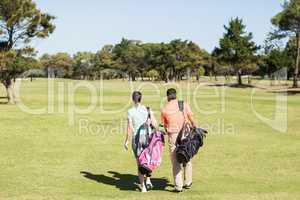 Rear view of couple carrying golf bags