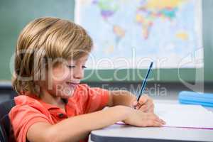 Smiling boy writing on book in classroom