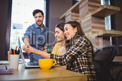 Coworkers smiling while pointing at laptop on desk
