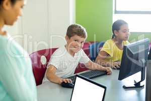Boy with classmate and teacher using computers