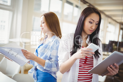 Female colleagues holding files and mobile phone in office