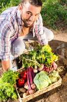 Portrait of happy gardener crouching with vegetables at garden