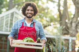 Male gardener holding vegetables crate outside greenhouse