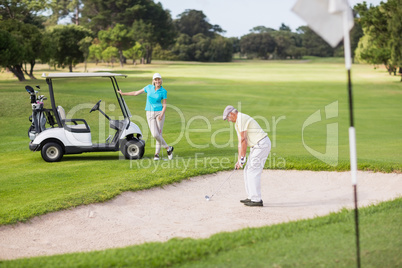 Golfer playing on sand trap by woman