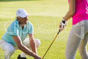 Mature golfer man crouching while teaching woman
