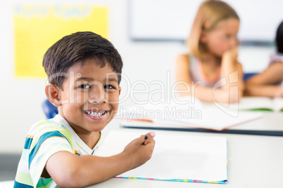 Boy writing on book against classmate