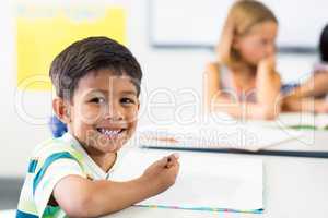 Boy writing on book against classmate