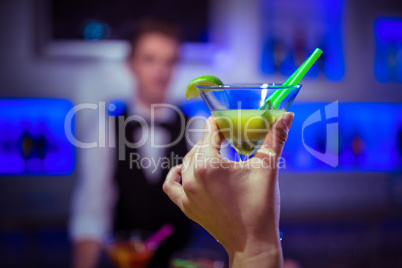 Cropped hand of customer holding cocktail glass against bartende