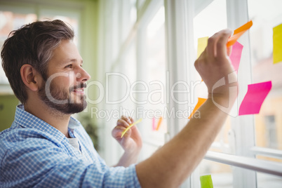 Happy businessman sticking adhesive notes on window at office