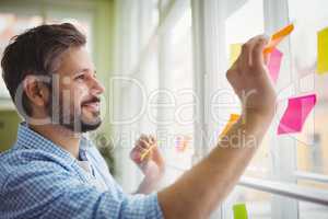 Happy businessman sticking adhesive notes on window at office