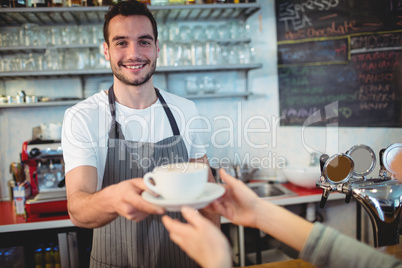 Portrait of confident waiter serving coffee to customer at cafe