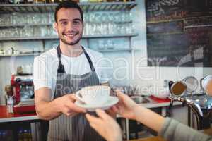 Portrait of confident waiter serving coffee to customer at cafe