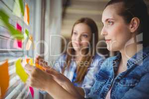 Businesswomen sticking adhesive notes on window in office