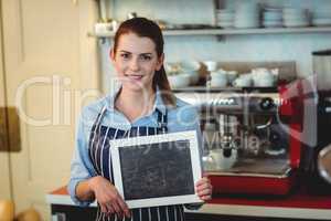 Portrait of happy barista holding blank chalkboard at cafe