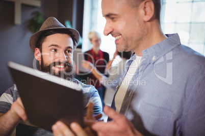 Happy male colleagues discussing over digital tablet