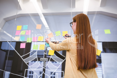 Businesswoman writing on multi colored sticky notes on glass