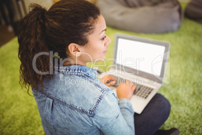 Businesswoman using laptop while sitting on carpet in office