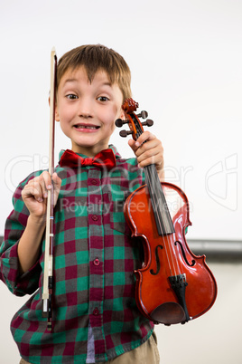 Cute boy holding violin with bow in classroom