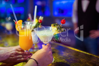 Cropped image of customers holding cocktail glasses by bartender