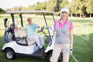 Smiling mature woman standing by man in golf buggy