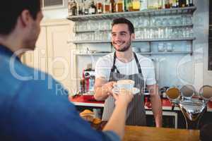 Happy waiter giving coffee to customer at cafe